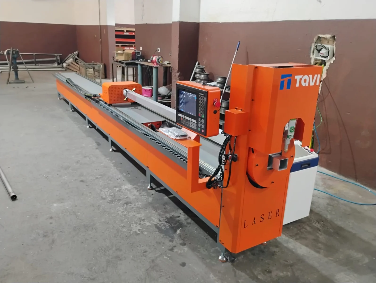 Equipamento de corte a laser de tubos com estrutura laranja no interior da fábrica Aladin